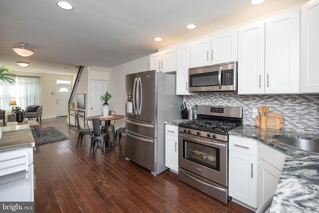 kitchen with appliances with stainless steel finishes, backsplash, dark stone countertops, dark hardwood / wood-style floors, and white cabinetry