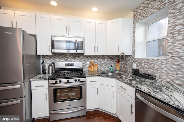 kitchen with decorative backsplash, stainless steel appliances, dark stone countertops, white cabinets, and dark hardwood / wood-style floors