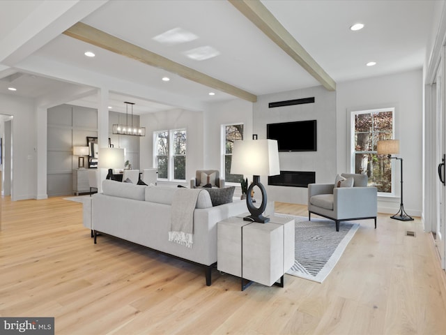 living room featuring a fireplace, beamed ceiling, light hardwood / wood-style floors, and an inviting chandelier