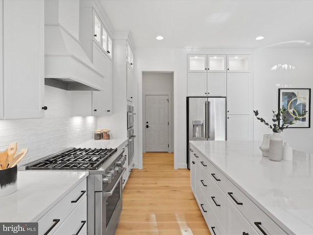 kitchen featuring light wood-type flooring, light stone counters, custom exhaust hood, high quality appliances, and white cabinets