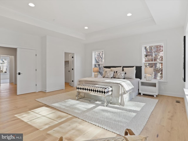 bedroom featuring a tray ceiling, multiple windows, and light wood-type flooring