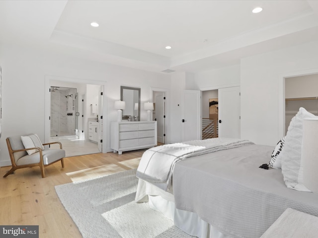 bedroom with a tray ceiling, ensuite bathroom, a closet, and light wood-type flooring