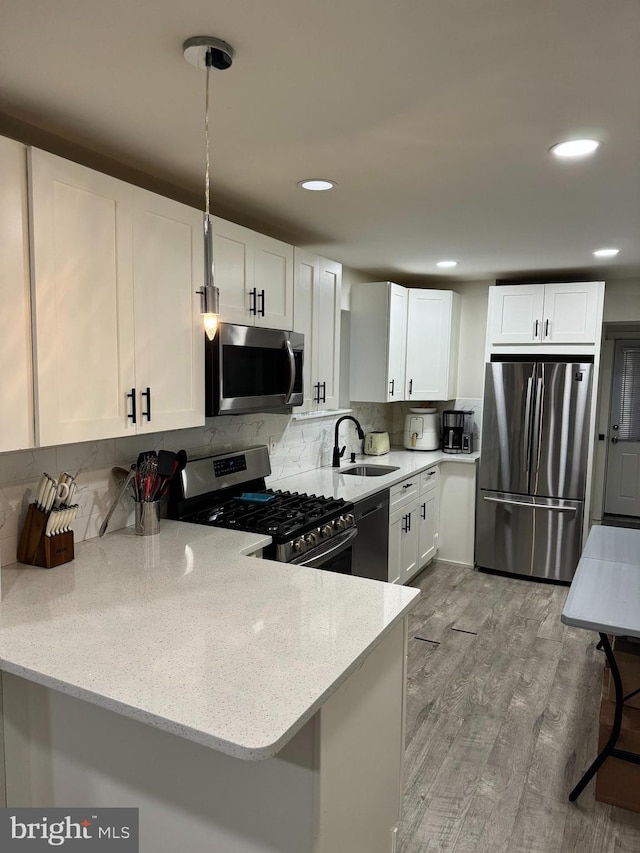 kitchen featuring stainless steel appliances, light hardwood / wood-style floors, kitchen peninsula, sink, and white cabinetry