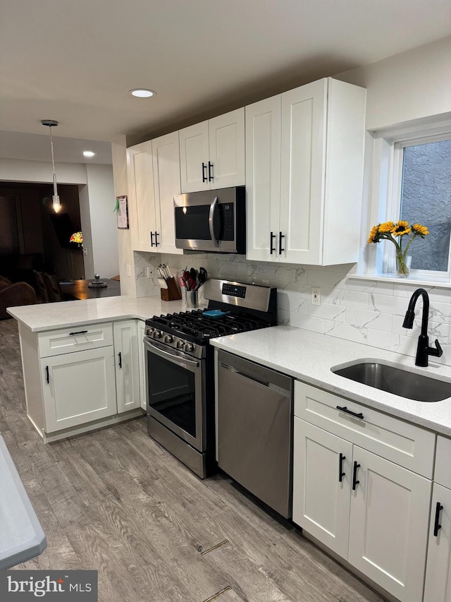 kitchen with sink, kitchen peninsula, appliances with stainless steel finishes, white cabinets, and pendant lighting