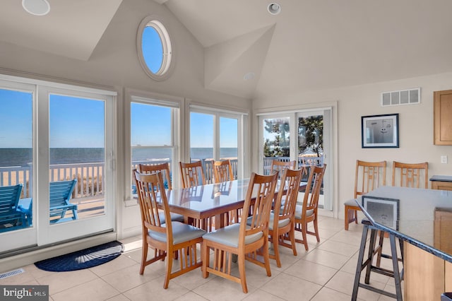 dining space with a water view, lofted ceiling, and light tile patterned floors