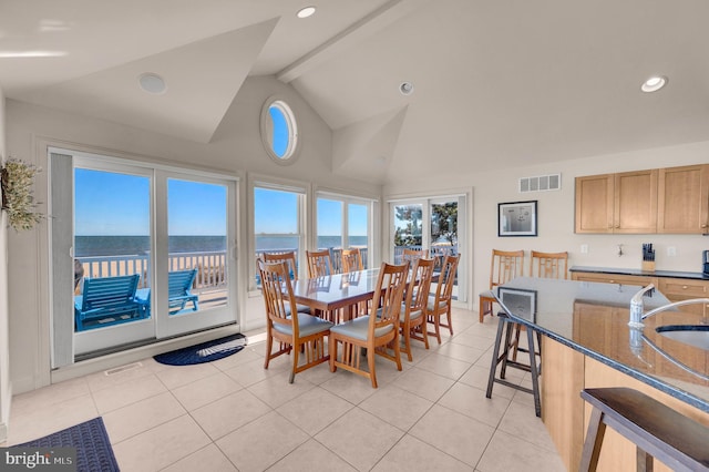 dining space with sink, a water view, lofted ceiling with beams, and light tile patterned floors