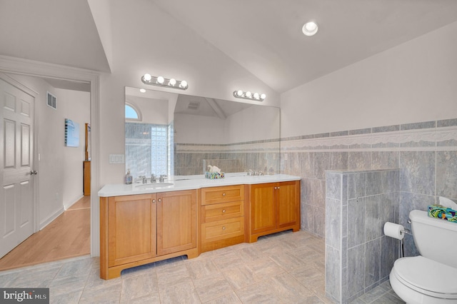 bathroom featuring vaulted ceiling, vanity, tile walls, and toilet