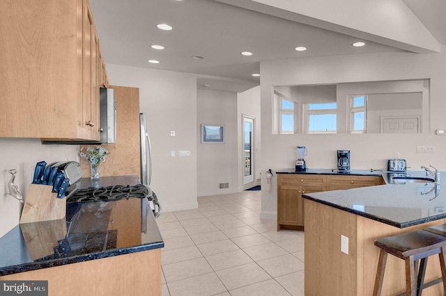 kitchen with kitchen peninsula, a breakfast bar, dark stone counters, and sink