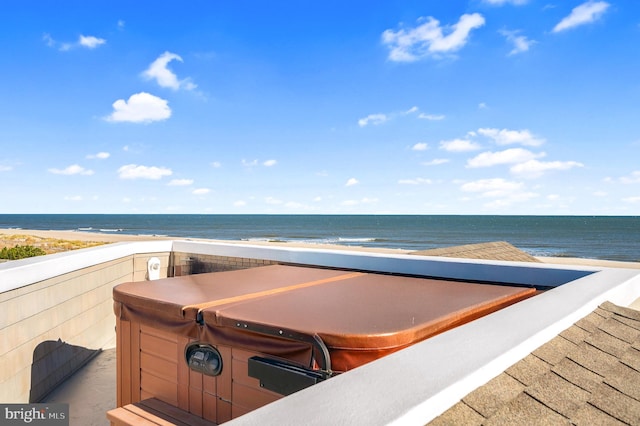 view of patio / terrace with a beach view, a water view, and a hot tub