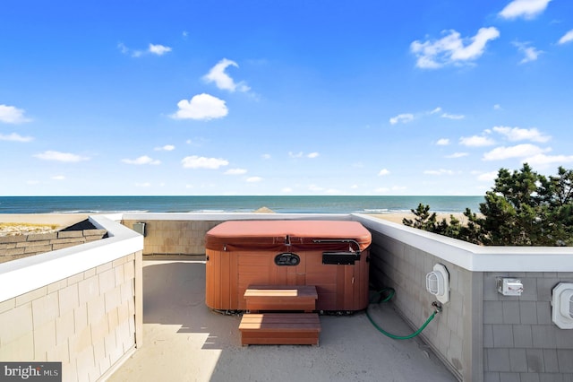 view of patio with a beach view, a water view, and a hot tub