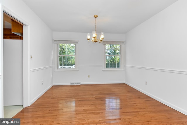 empty room with a healthy amount of sunlight, light hardwood / wood-style floors, and an inviting chandelier