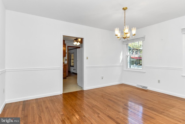 spare room with ceiling fan with notable chandelier and wood-type flooring