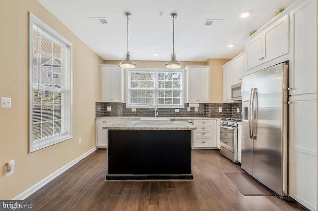 kitchen with a healthy amount of sunlight, decorative light fixtures, appliances with stainless steel finishes, and a center island