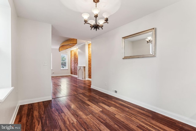 spare room featuring dark wood-type flooring and a chandelier