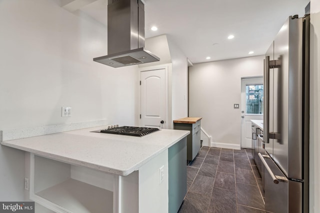 kitchen with island exhaust hood, appliances with stainless steel finishes, light stone countertops, and kitchen peninsula