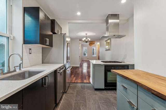 kitchen with wooden counters, island range hood, sink, black oven, and decorative light fixtures