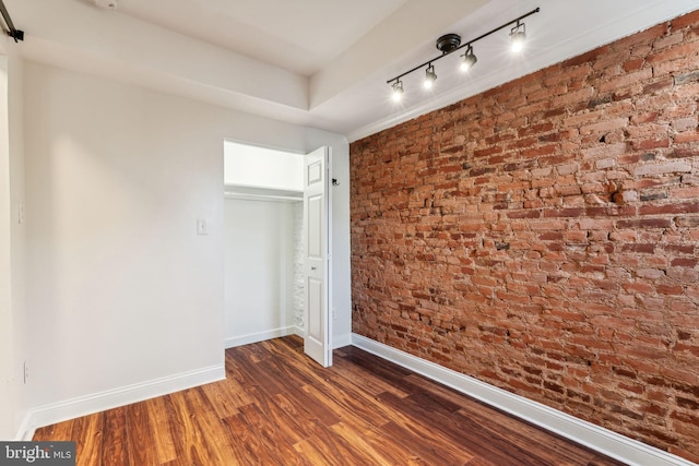 spare room with rail lighting, brick wall, and dark wood-type flooring