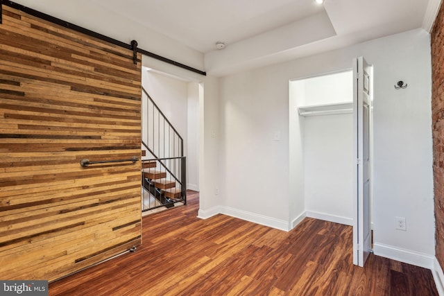 unfurnished bedroom with a barn door, dark hardwood / wood-style floors, and a closet