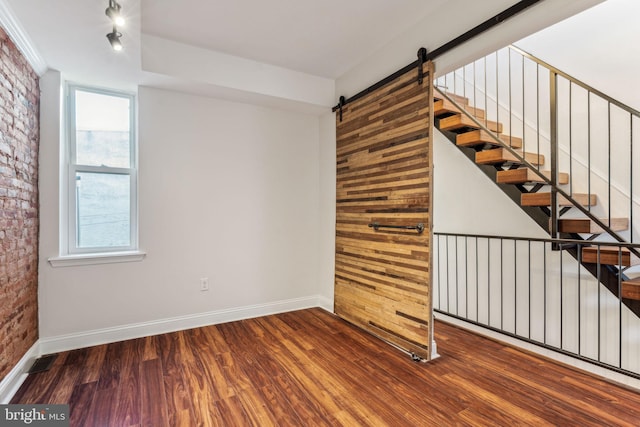 unfurnished room with a barn door, hardwood / wood-style flooring, and brick wall