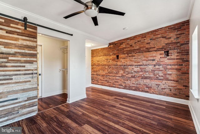 unfurnished room featuring dark wood-type flooring, a barn door, ceiling fan, crown molding, and brick wall