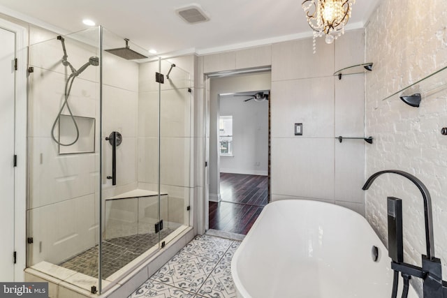 bathroom featuring plus walk in shower, hardwood / wood-style flooring, ornamental molding, and ceiling fan with notable chandelier