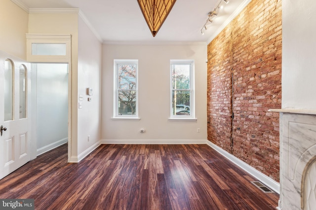 empty room featuring dark wood-type flooring, brick wall, track lighting, and ornamental molding