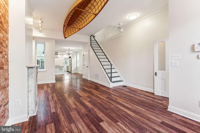 foyer entrance with ornamental molding, a towering ceiling, dark wood-type flooring, and a chandelier