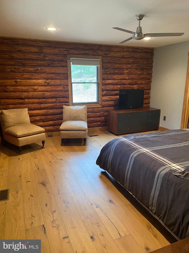 bedroom featuring wood-type flooring, rustic walls, and ceiling fan