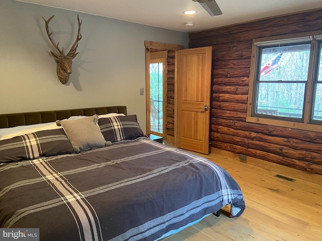 bedroom featuring hardwood / wood-style floors, rustic walls, and ceiling fan