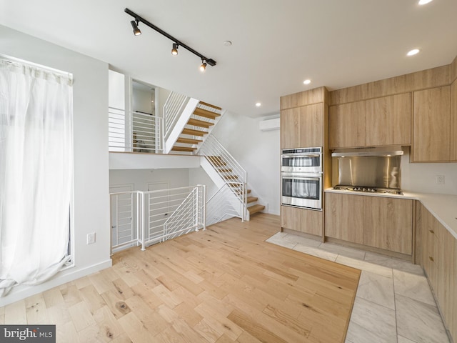 kitchen featuring a wall unit AC, light brown cabinetry, light wood-type flooring, and appliances with stainless steel finishes