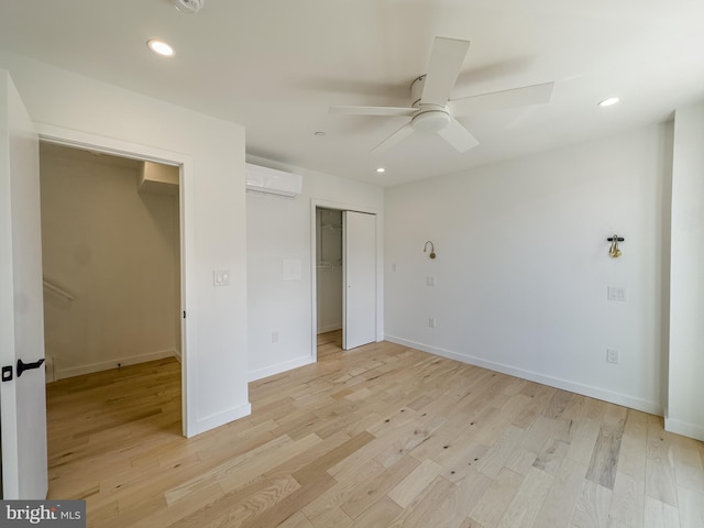 unfurnished bedroom featuring a wall mounted AC, light hardwood / wood-style flooring, ceiling fan, and a closet