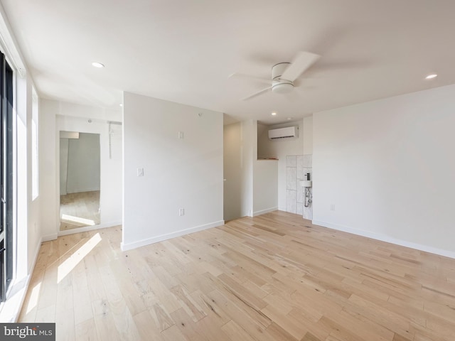 unfurnished room featuring a wall unit AC, light hardwood / wood-style floors, and ceiling fan