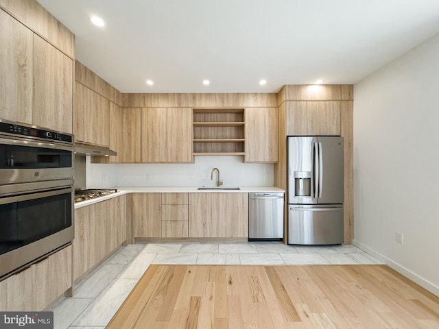 kitchen featuring stainless steel appliances, sink, light brown cabinets, light wood-type flooring, and exhaust hood