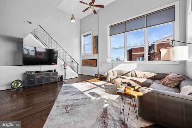 living room with a towering ceiling, ceiling fan, and dark wood-type flooring