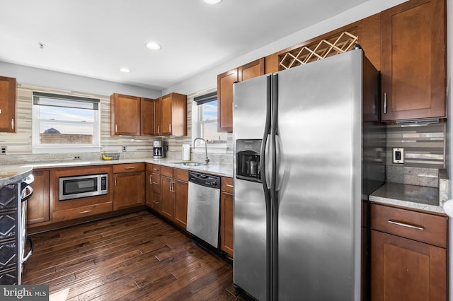 kitchen with appliances with stainless steel finishes, backsplash, light stone counters, sink, and dark hardwood / wood-style floors