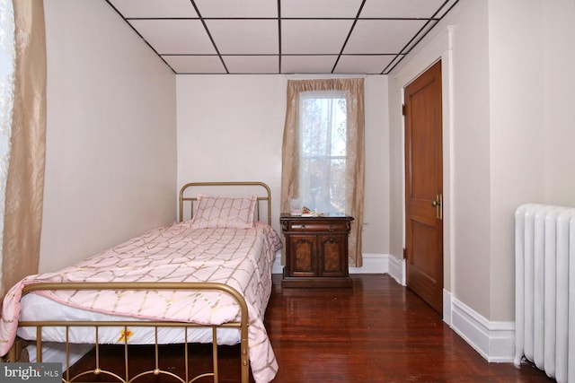 bedroom with a paneled ceiling, radiator heating unit, and dark wood-type flooring