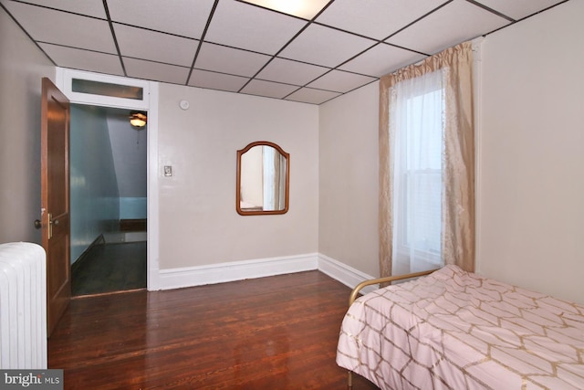 unfurnished bedroom with a paneled ceiling, dark hardwood / wood-style flooring, and radiator heating unit