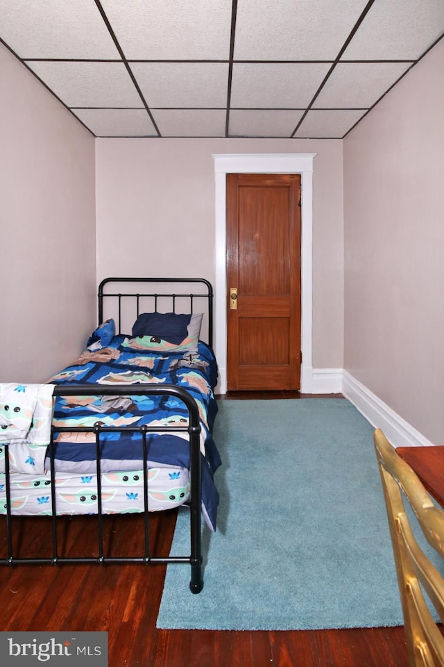 bedroom with a drop ceiling and dark wood-type flooring