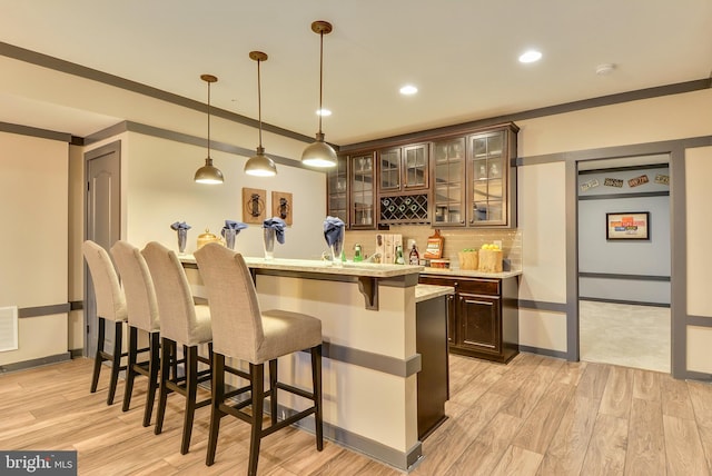 bar with backsplash, dark brown cabinets, hanging light fixtures, and light wood-type flooring