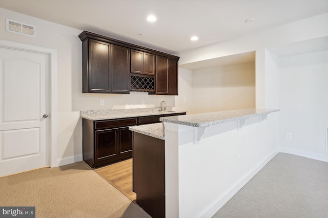 bar featuring dark brown cabinets, light colored carpet, light stone countertops, and sink