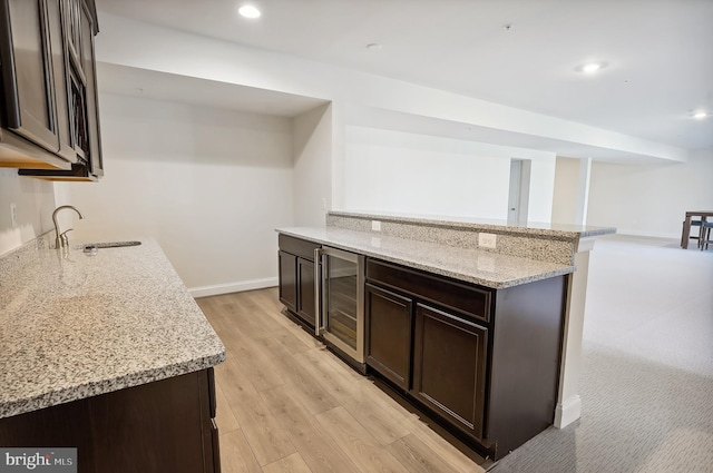 kitchen featuring sink, light hardwood / wood-style flooring, light stone countertops, dark brown cabinetry, and beverage cooler