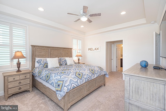 carpeted bedroom with ceiling fan, a raised ceiling, ornamental molding, and ensuite bath