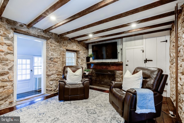 sitting room with a stone fireplace, beamed ceiling, wood-type flooring, and radiator