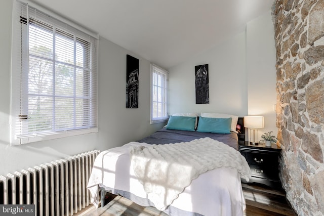 bedroom featuring radiator heating unit, vaulted ceiling, multiple windows, and hardwood / wood-style floors