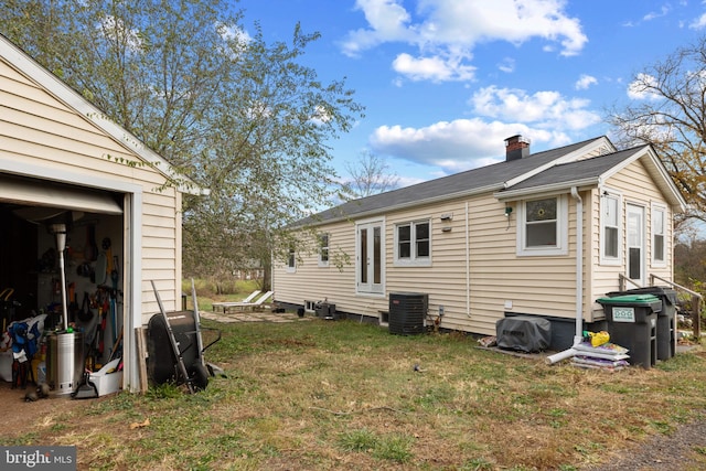 rear view of property featuring a garage, a yard, and central AC