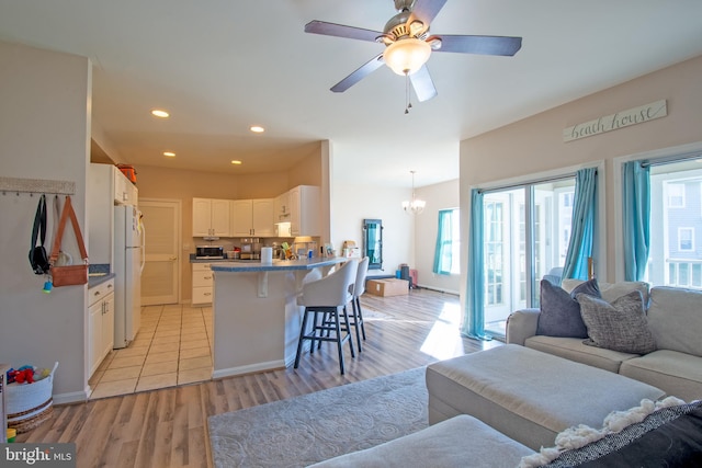 kitchen with white cabinets, kitchen peninsula, a breakfast bar area, white fridge, and light hardwood / wood-style flooring