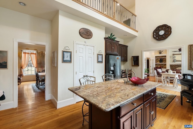 kitchen featuring dark brown cabinetry, a kitchen bar, an island with sink, a towering ceiling, and fridge with ice dispenser