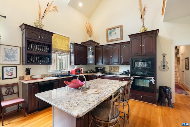 kitchen featuring dark brown cabinetry, black appliances, a kitchen island with sink, a breakfast bar, and light hardwood / wood-style flooring