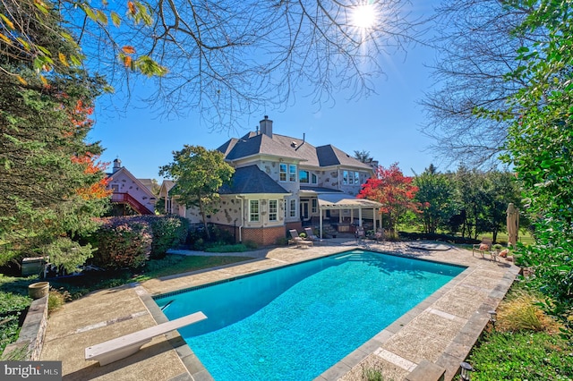 view of swimming pool featuring a diving board and a patio