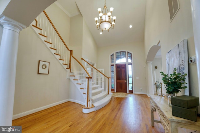 foyer with a notable chandelier, light hardwood / wood-style floors, ornate columns, and a high ceiling